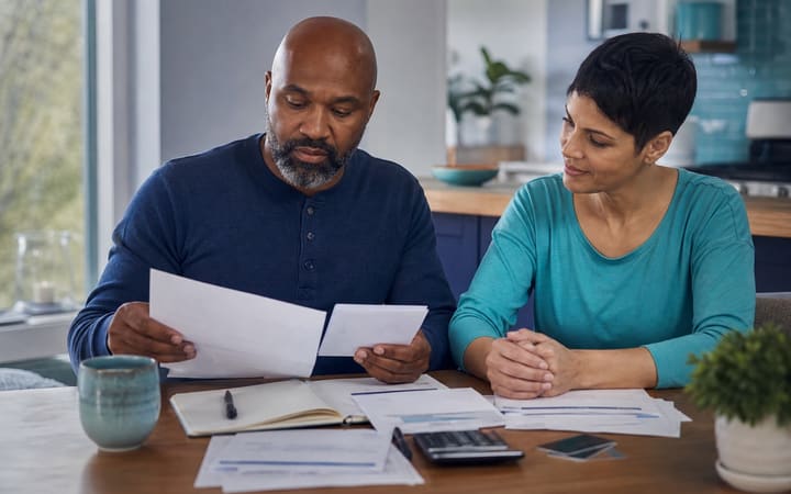 Person calmly reviewing bills with a notebook, calculator and laptop at a tidy kitchen table