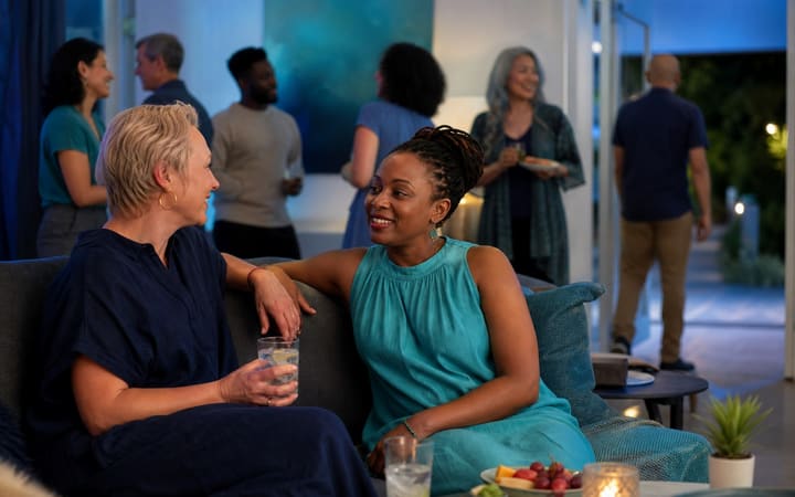 A person holding sparkling water while talking with a supportive friend at a relaxed social gathering